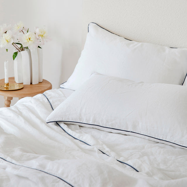 A close up of a bed dressed in White and Navy Piped bed linen