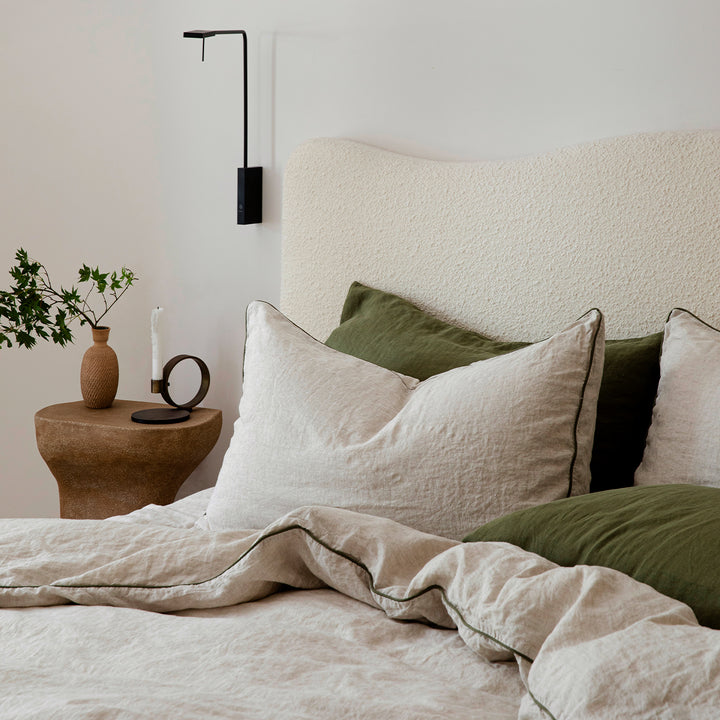 A cream bed dressed in Natural and Forest Piped bed linen, paired with pillowcases in Forest