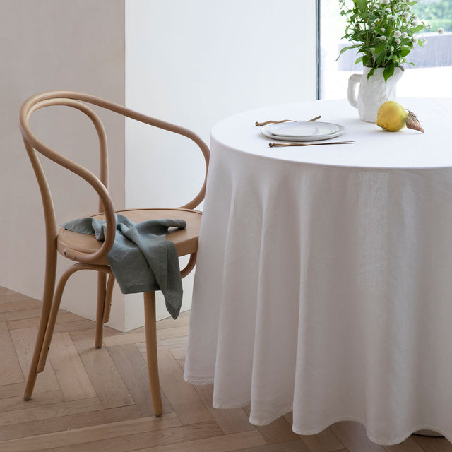 A table dressed in a White Linen Tablecloth, styled with a wooden chair and napkin