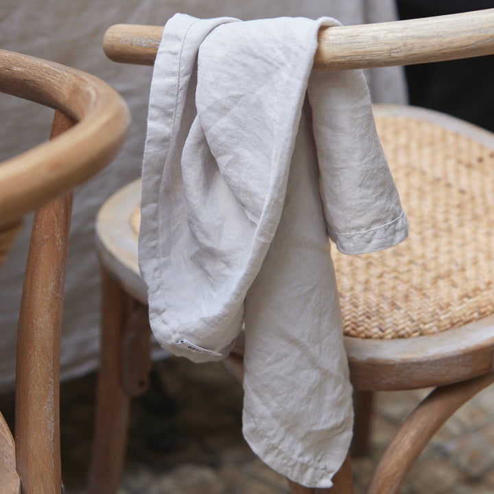 Close up of a Linen Napkin in Smoke Grey hanging from the back of a wooden chair.