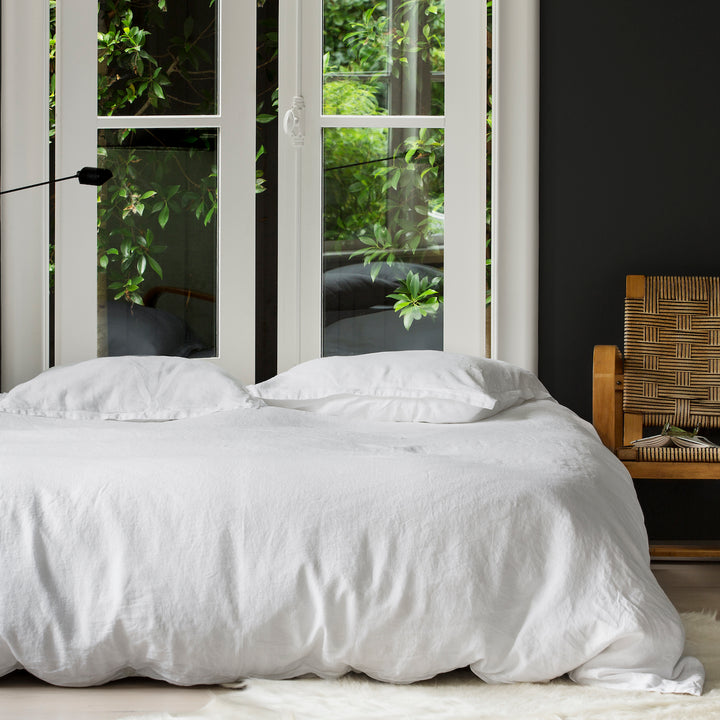 A bed dressed with White bedlinen, contrasting charcoal walls and large windows. Sizes: Queen, King