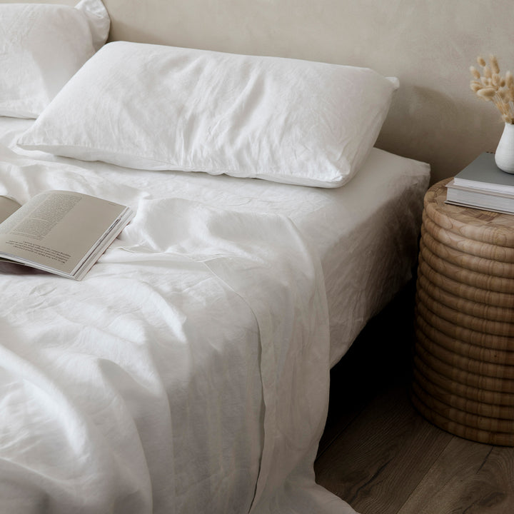A bed dressed in White bedlinen styled with books and a bedside table.