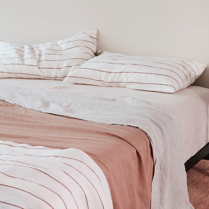 A bed dressed in Blush, Smoke Grey, Fawn and Cedar Stripe bed linen