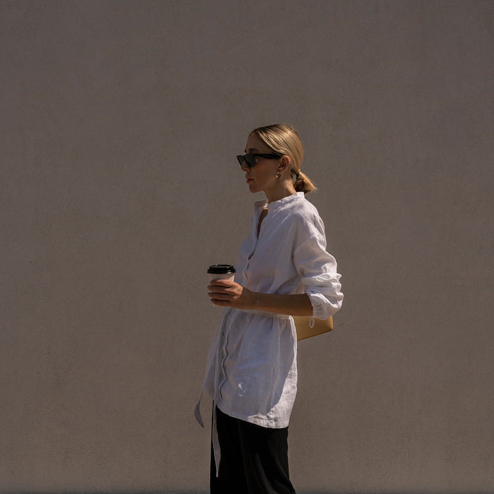 A woman wearing a Cristi Linen Shirt in White holding a takeaway coffee