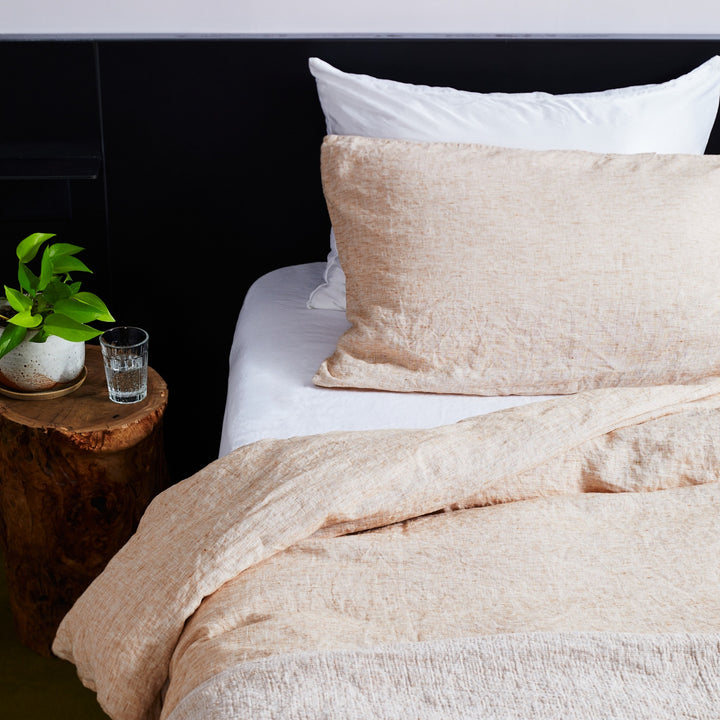  A close up of a bed dressed in Cinnamon and White bed linen, styled with a wooden bedside table and a pot plant