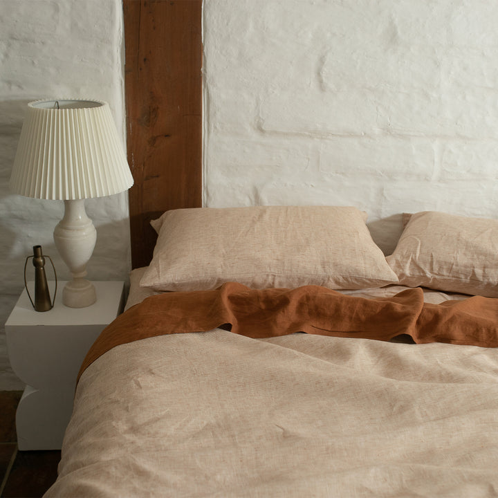 A bed dressed in Cinnamon and Cedar bed linen, styled with a modern white bedside table and cream lamp. Sizes: Queen, King