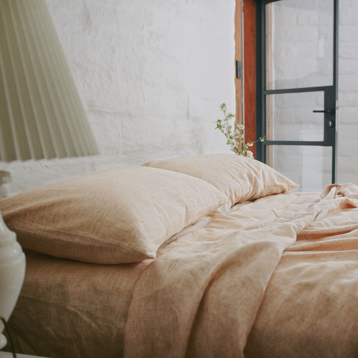 A bed dressed in Cinnamon bedlinen styled with a side table and glass door.