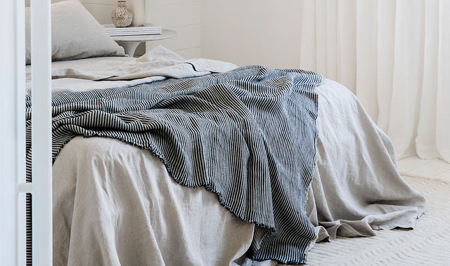A bed styled with a Linen Duvet Cover Set in Natural. Draped on top of the bed is the Mira Linen Bedcover in Ellis Stripe.