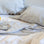 A close up of a bed styled with a Linen Duvet Cover and Set of 2 Linen Pillowcases in Pinstripe and Linen Flat Sheet with Border and Linen Fitted Sheet in White. On top of the bed is a gray plate with a glass of water on top. Next to the plate is a lemon.
