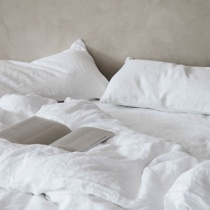 Bed styled with a White Linen Duvet Cover and Linen Sheet Set. On the bed there is a book lying open. Sizes: Queen, King