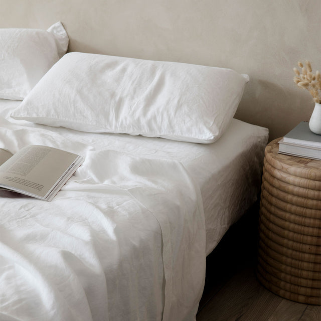 A bed dressed in White bed linen, styled with a wooden bedside table and book. Sizes: Queen, King, California King