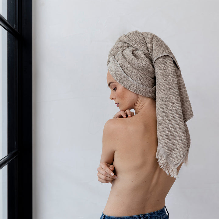 A model is standing with her back to the camera. She isn't wearing a shirt, and has a Pure Linen Bath Towel in Natural wrapped around her hair. 